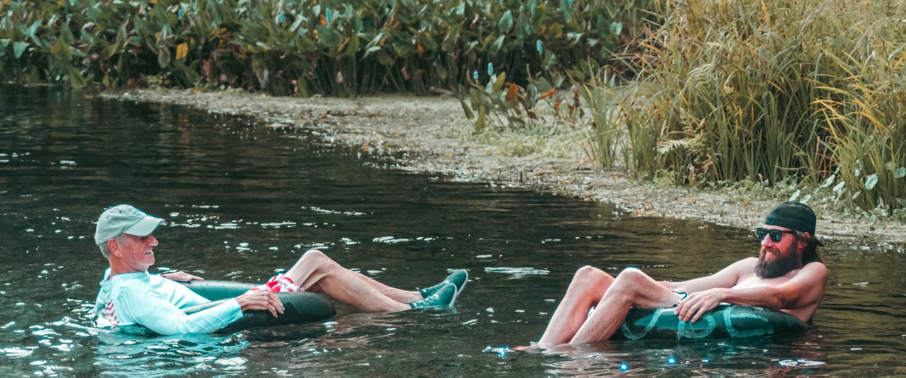 Two men leisurely floating in a calm river, basking in the warm sunlight on a relaxing afternoon.