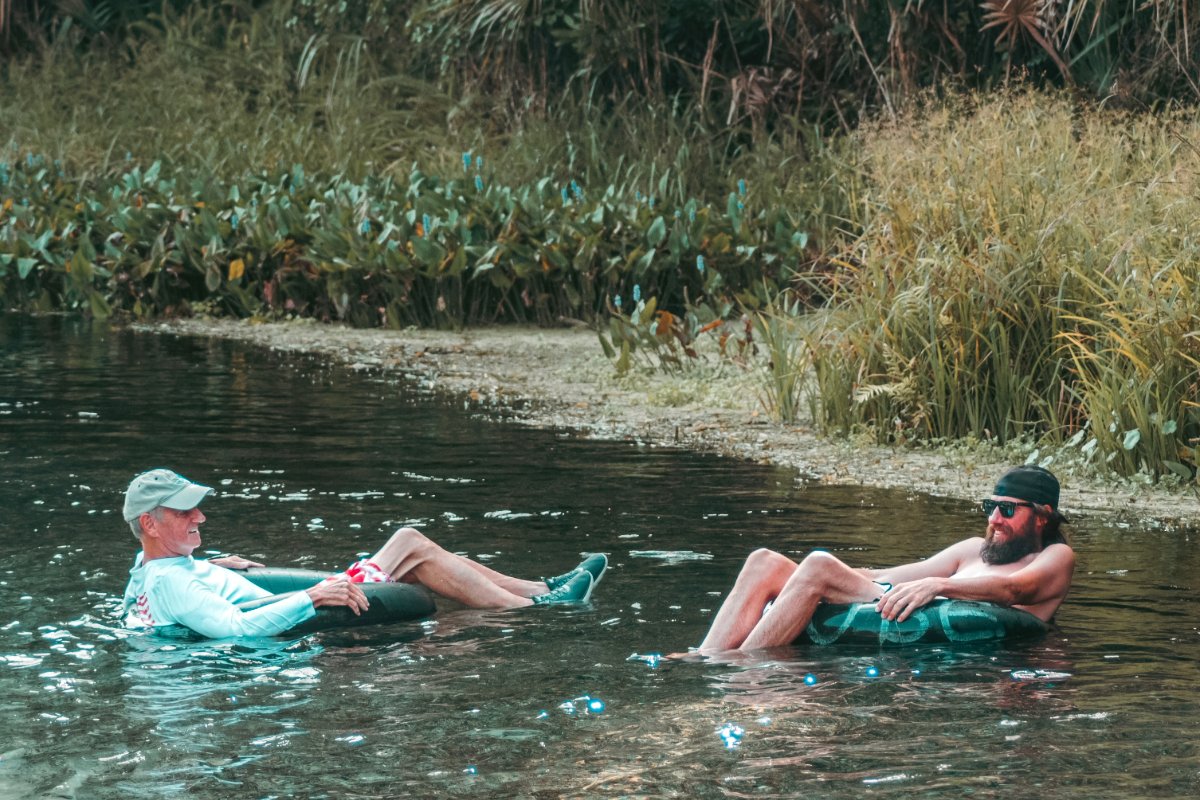 Two men leisurely floating in a calm river, basking in the warm sunlight on a relaxing afternoon.