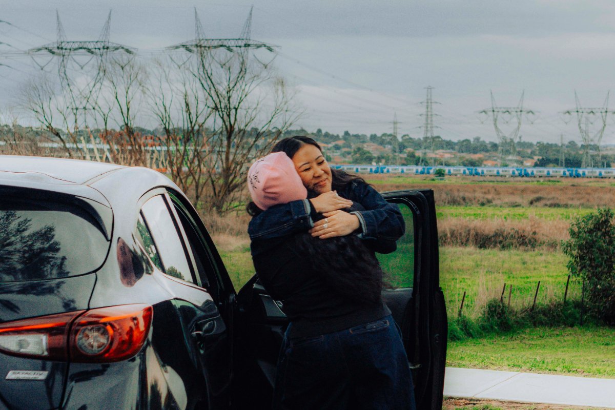 Two women hugging by a car, both looking happy.