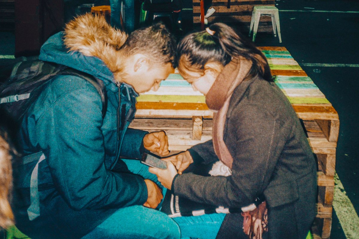 A pair of people scrolling on their phones while seated on a park bench.