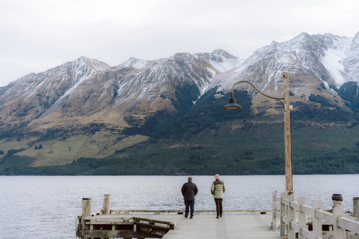 A couple walking on a pier with mountains in the background.