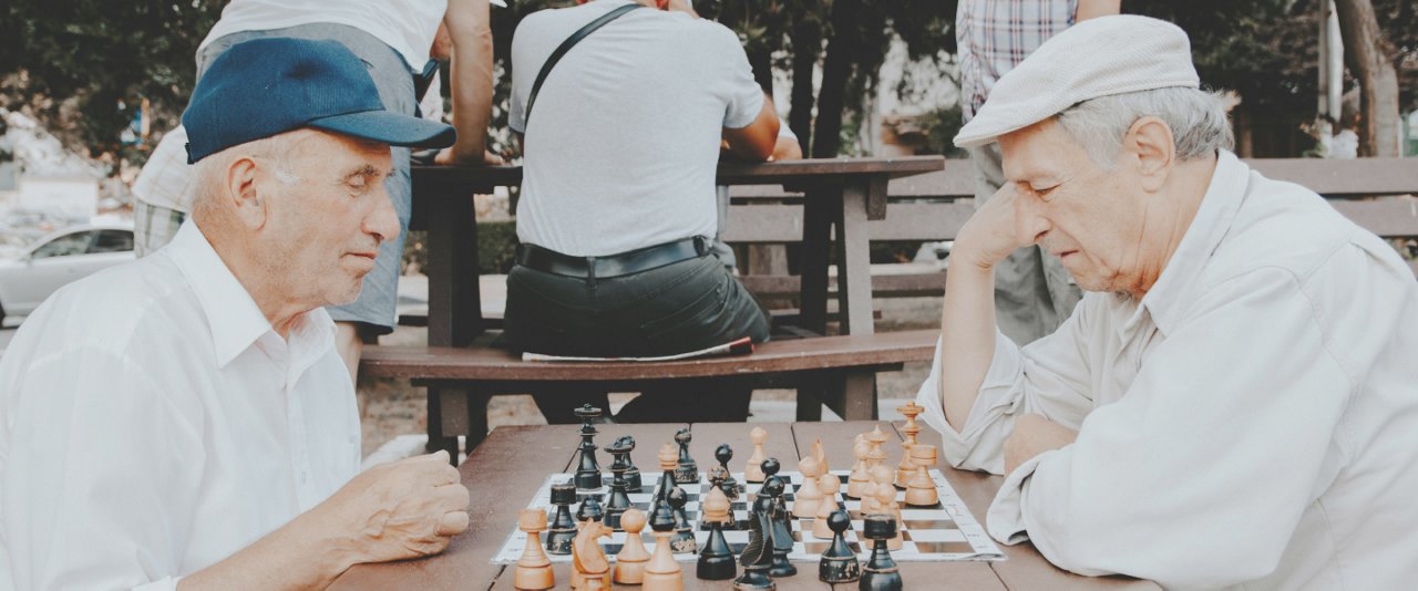 Two elderly men playing chess on a park bench.