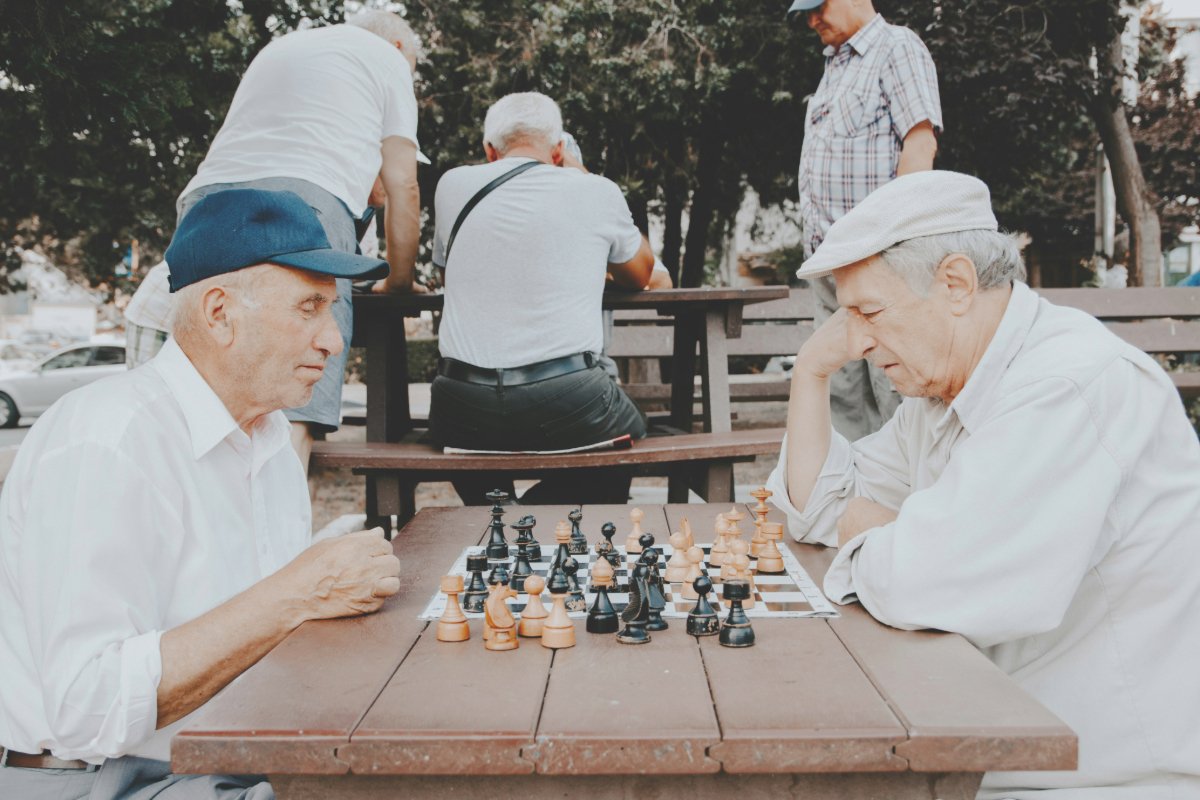 Two elderly men playing chess on a park bench.