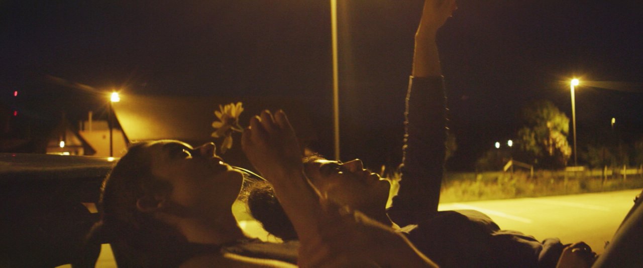 Two individuals lying on the car, looking up at the sky.