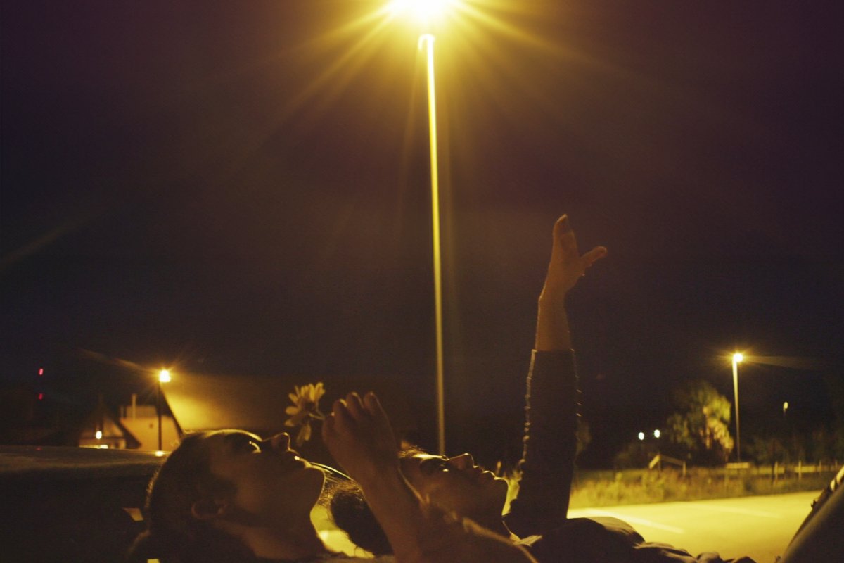 Two individuals lying on the car, looking up at the sky.