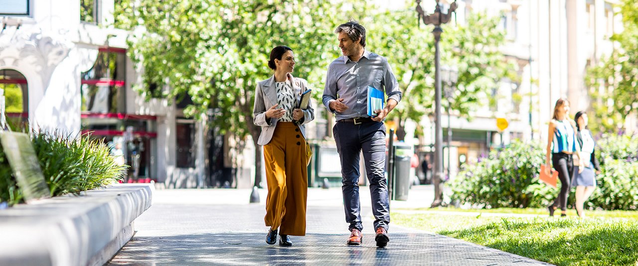 An office worker and a co-worker strolling on the sidewalk outside.