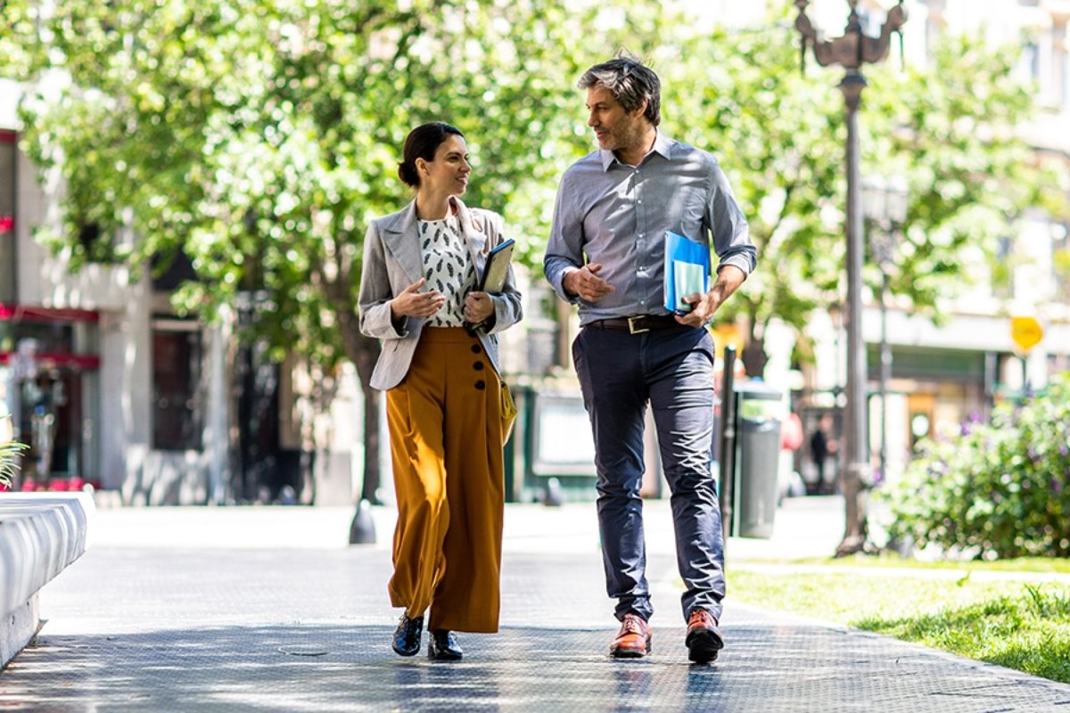 An office worker and a co-worker strolling on the sidewalk outside.