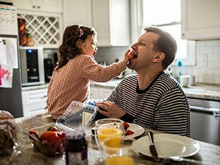 Daughter feeding dad laughing at kitchen table