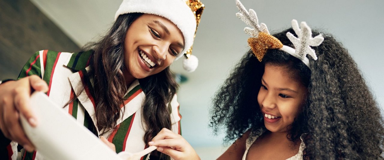 A woman and a girl in Santa hats joyfully open a gift together