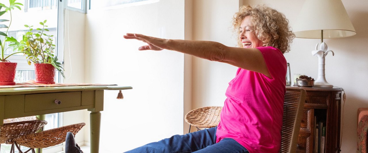 A woman seated on a chair, extending her arms overhead in a stretching pose for relaxation and flexibility.