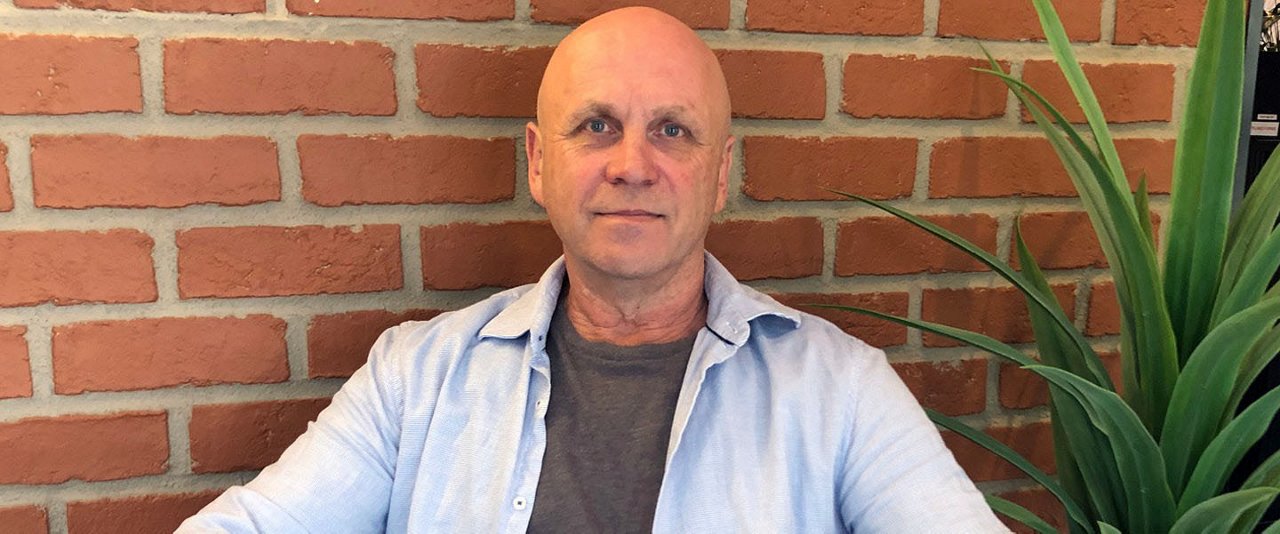 A  bald man seated against a textured brick wall,