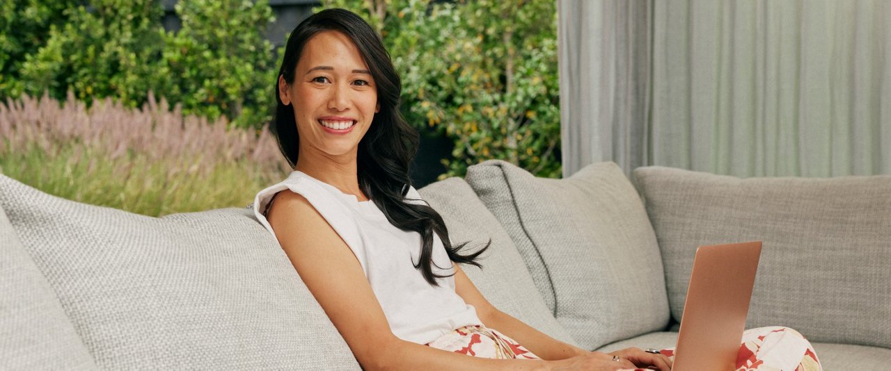 A woman seated on a couch, focused on her laptop