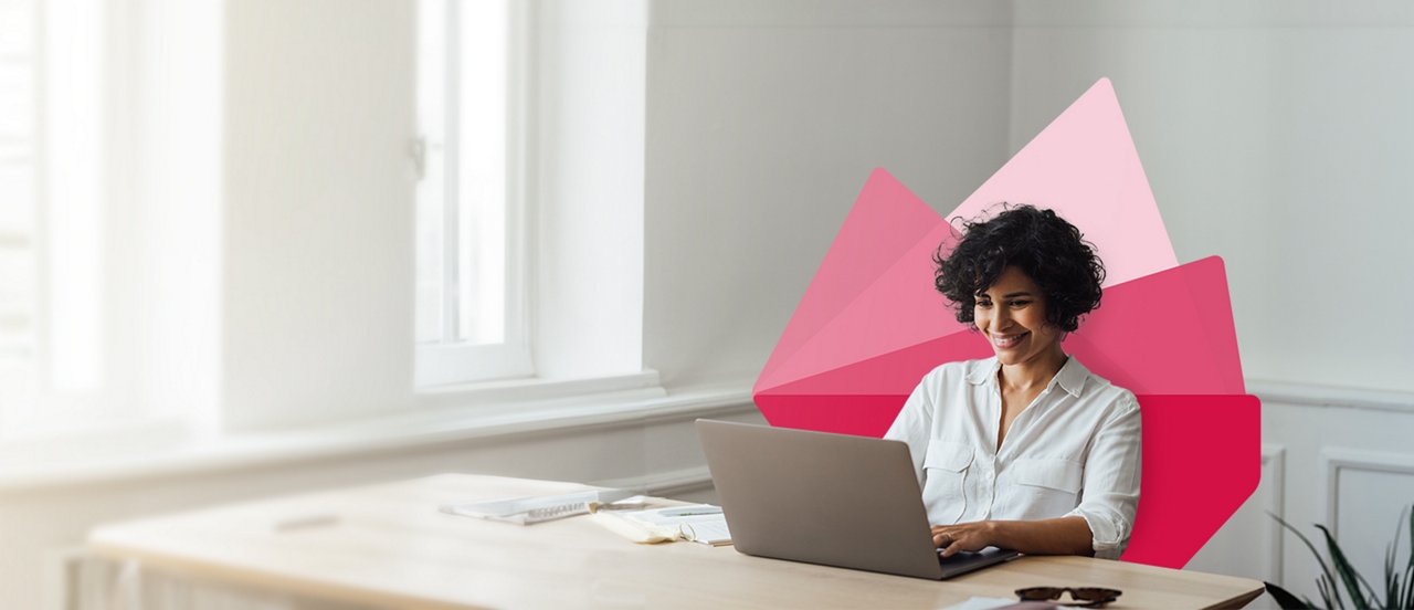 A woman seated at a desk, focused on her laptop, surrounded by a tidy workspace.