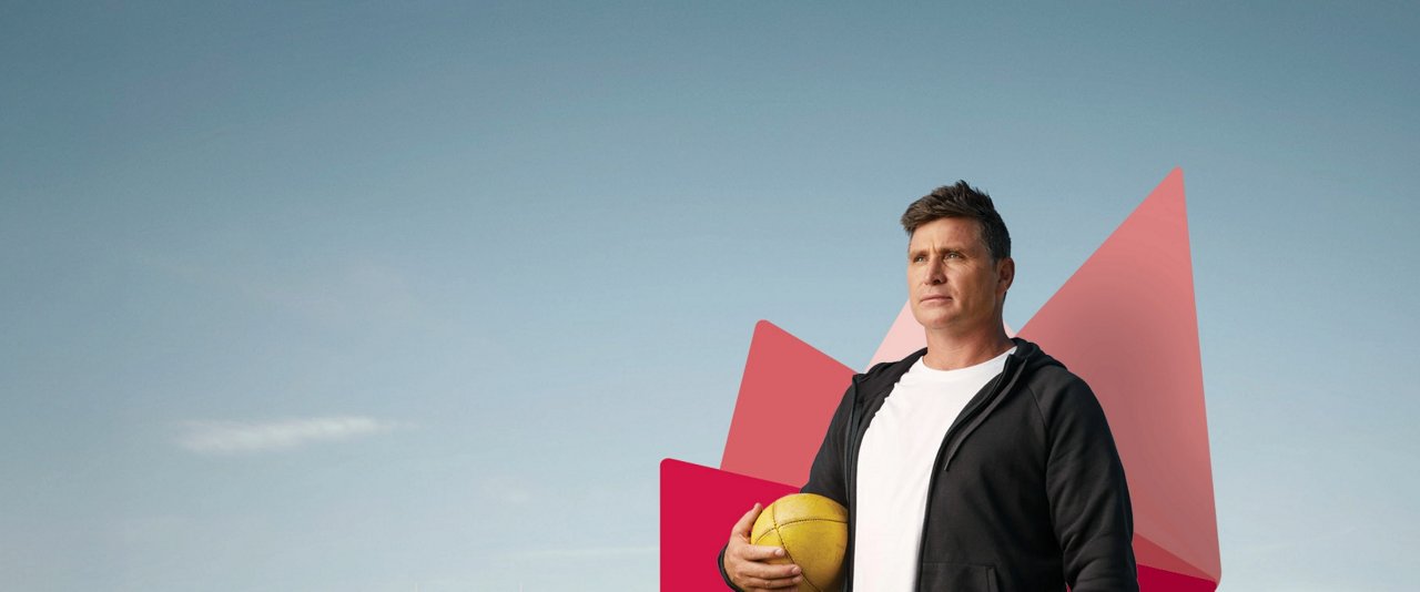 Shane Crawford, Australian former AFL player, stands confidently holding a football.