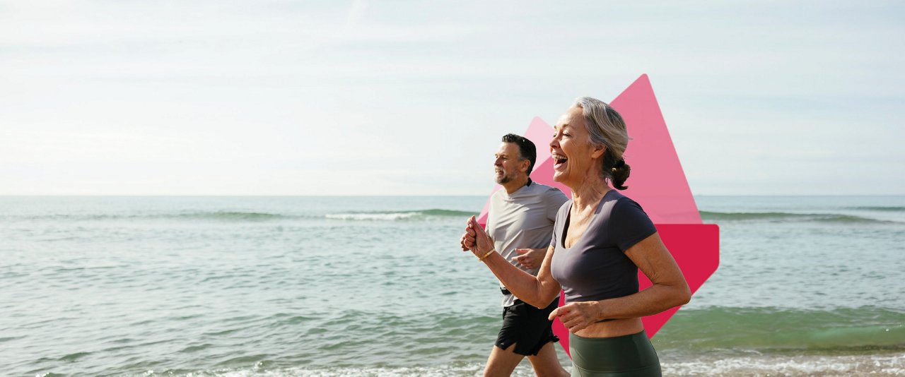 A man and woman joyfully run along the beach.