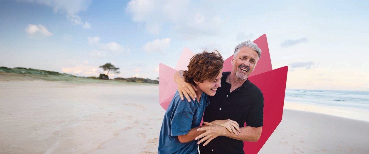 Two men embrace on a beach, surrounded by sand and waves