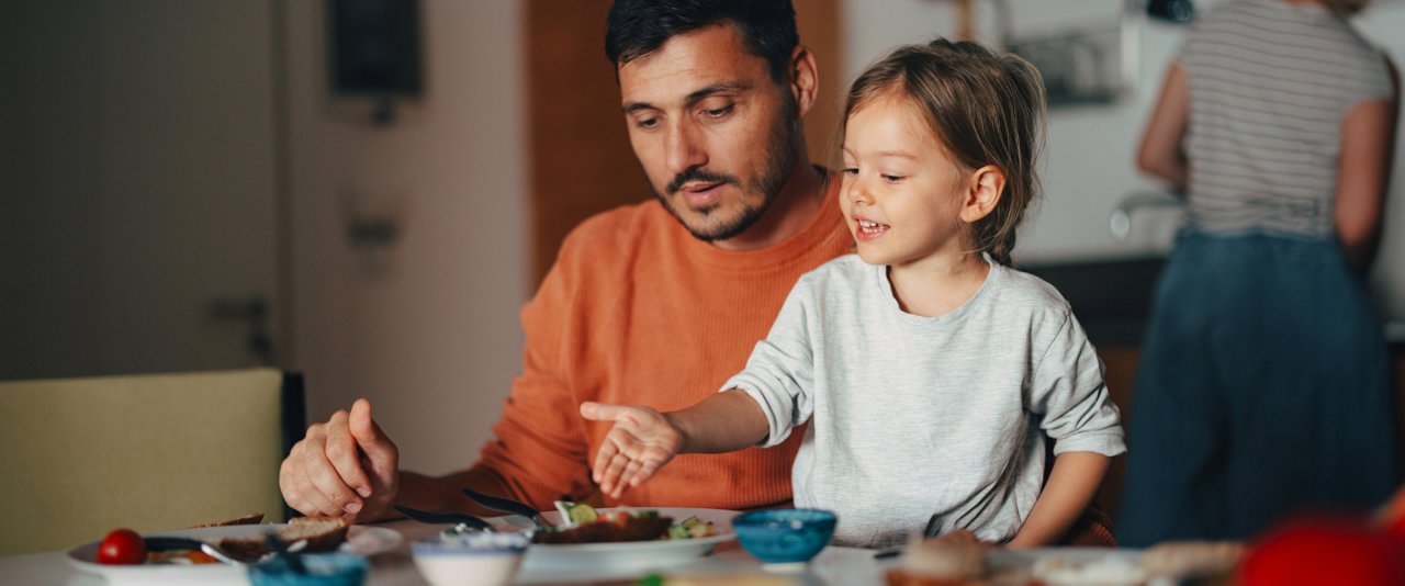 A man and a child share a meal together at a table, enjoying their time and food in a warm setting.