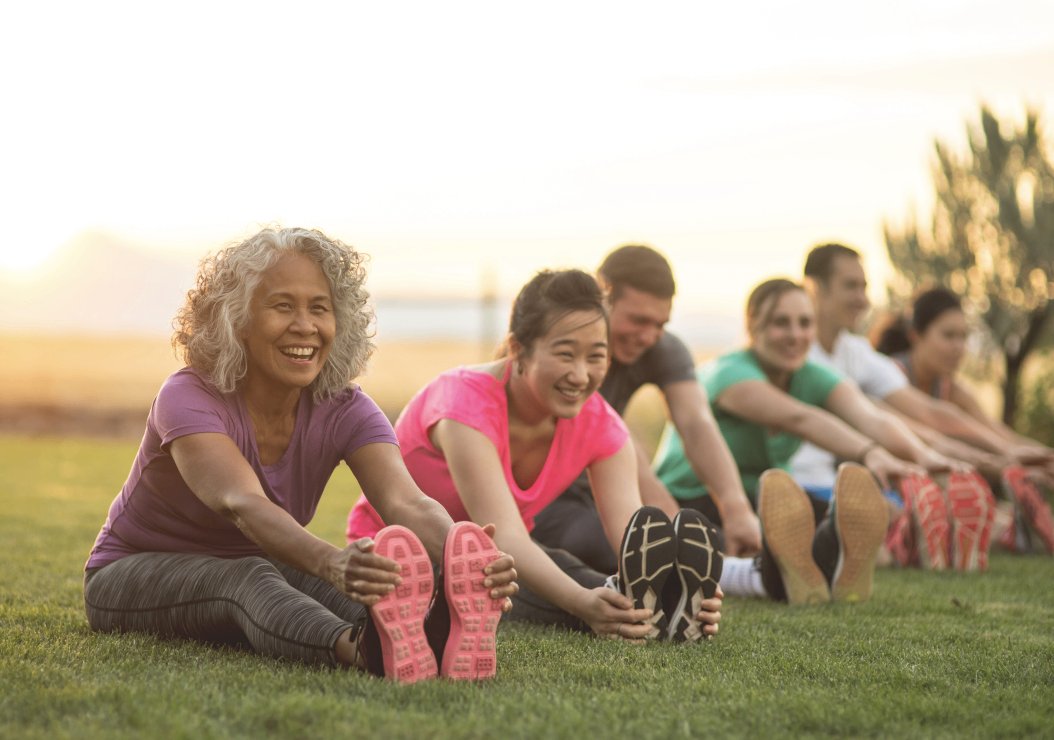 A diverse group of individuals performing stretching exercises on a grassy field under a clear blue sky.