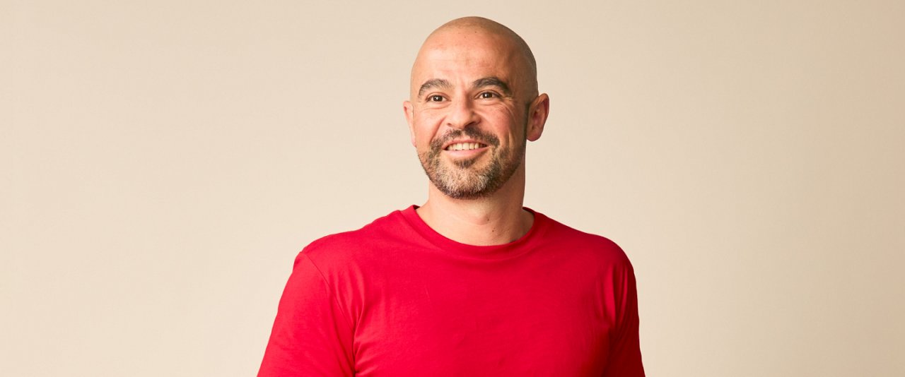 AIA Financial Wellbeing Advice Manager, Tristan Knowles, wearing a red shirt smiles warmly at the camera.