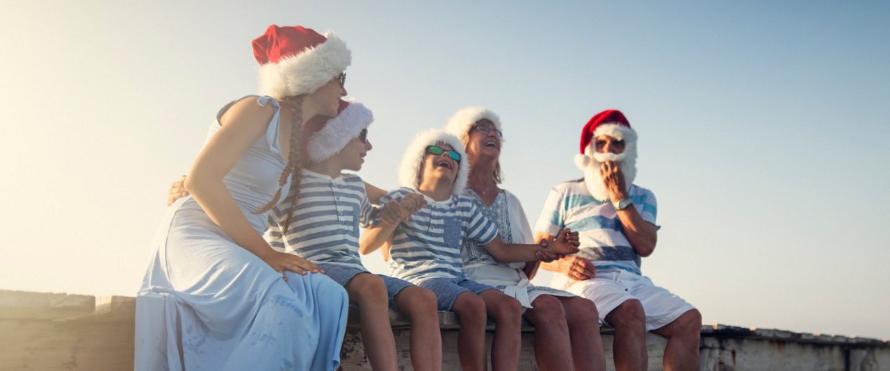 A family of four wearing Santa hats joyfully sits together on a wall, celebrating the festive season.