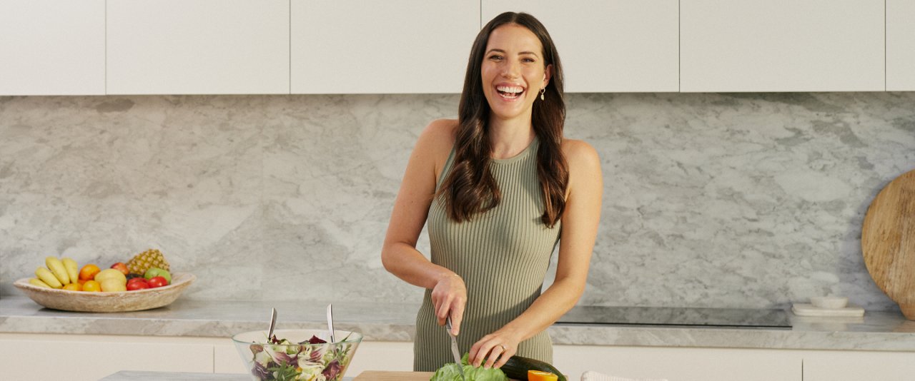 A woman is chopping vegetables on a cutting board in a well-lit kitchen.