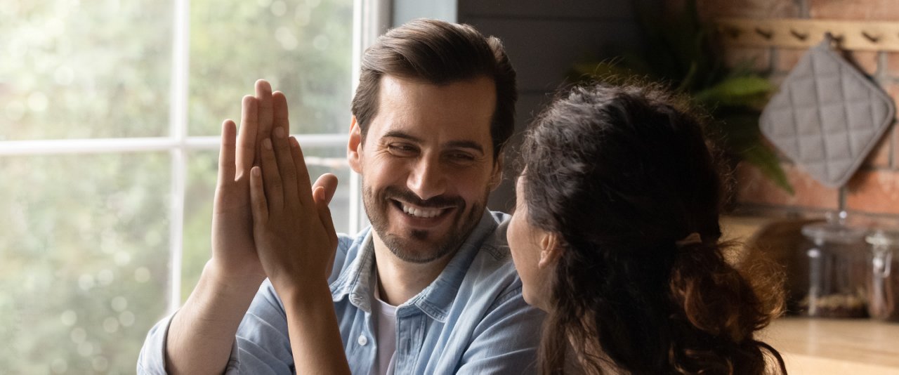 A man and woman at a table joyfully high-fiving each other, celebrating a shared moment of success.