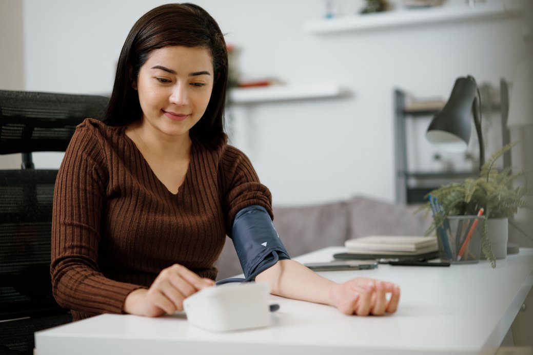 An Asian woman is using a blood pressure monitor to check her blood pressure at home.