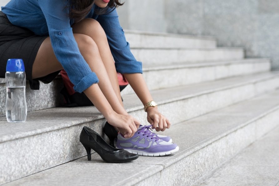 Woman in corporate attire changes from heels to running shoes