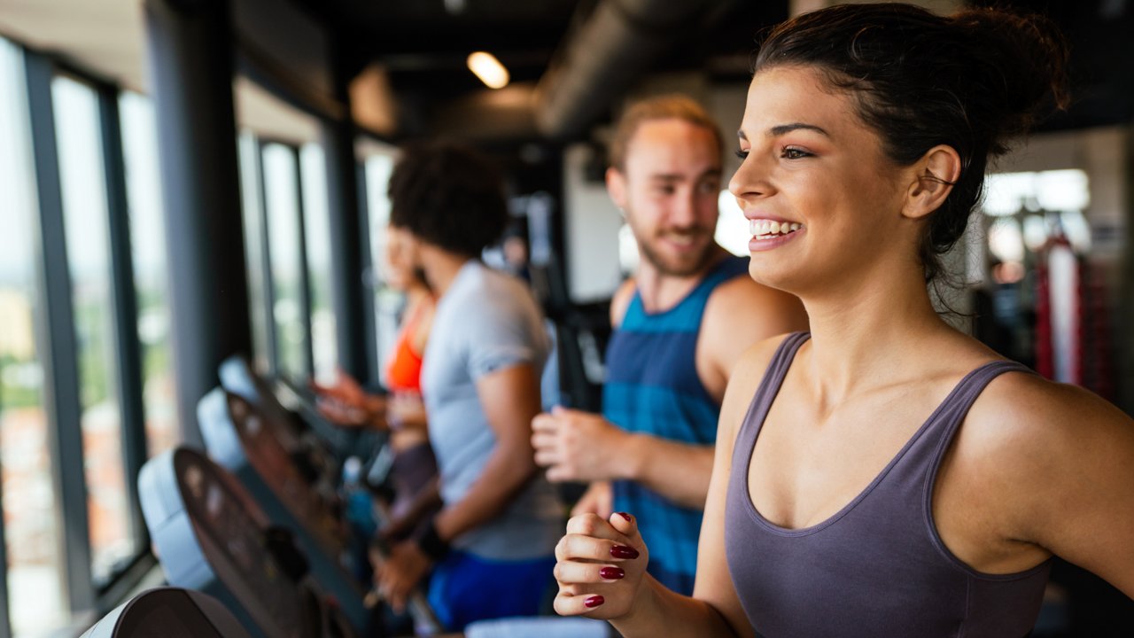A woman runs on a treadmill in a gym, surrounded by exercise machines