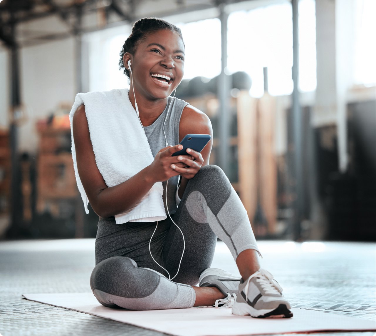 A woman seated on the floor, engaged with her phone while wearing headphones, immersed in her listening experience.