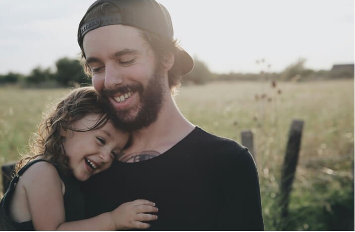 A man and a young girl embrace warmly in a sunlit field