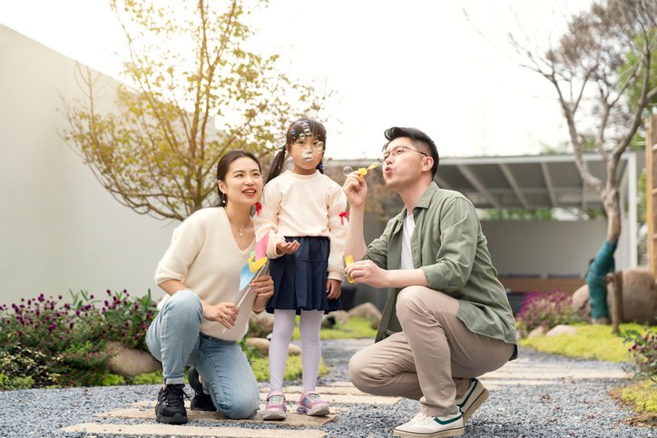 年輕父母與小女孩在戶外吹泡泡，象徵家庭建立初期的保障需求，強調孩子成長階段應規劃適合的醫療、危疾、教育及意外保險。