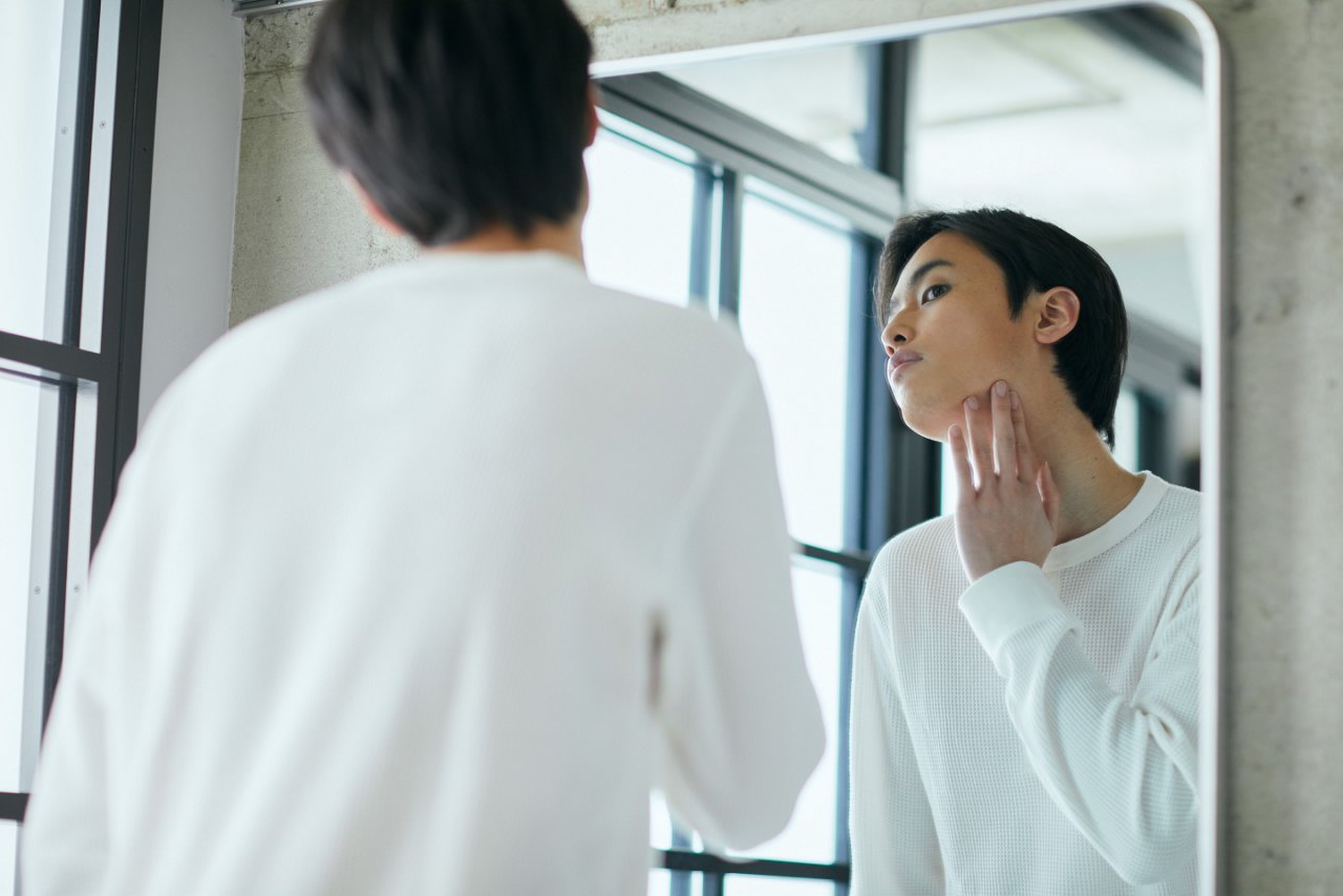 An Asian man uses his fingers to touch under the jaw and along the side of the neck, self-checking the neck lymph nodes for swelling or tenderness.