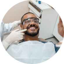 Man laying in dentist chair while smiling and inspecting his teeth