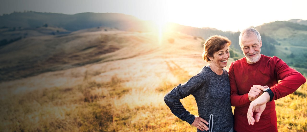 A senior couple stands in a field at sunset, surrounded by nature, reflecting a peaceful and loving relationship.