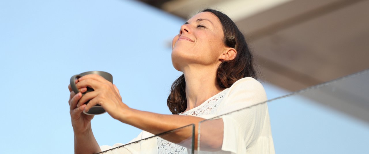 A woman stands on a balcony, holding a cup of coffee, enjoying the view and the morning ambiance.