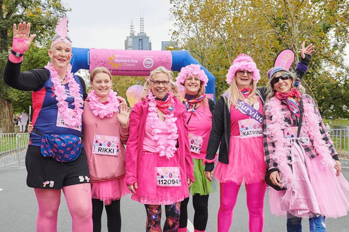 Six women at at the Mothers Day Classic fundraiser dressed in pink and waving