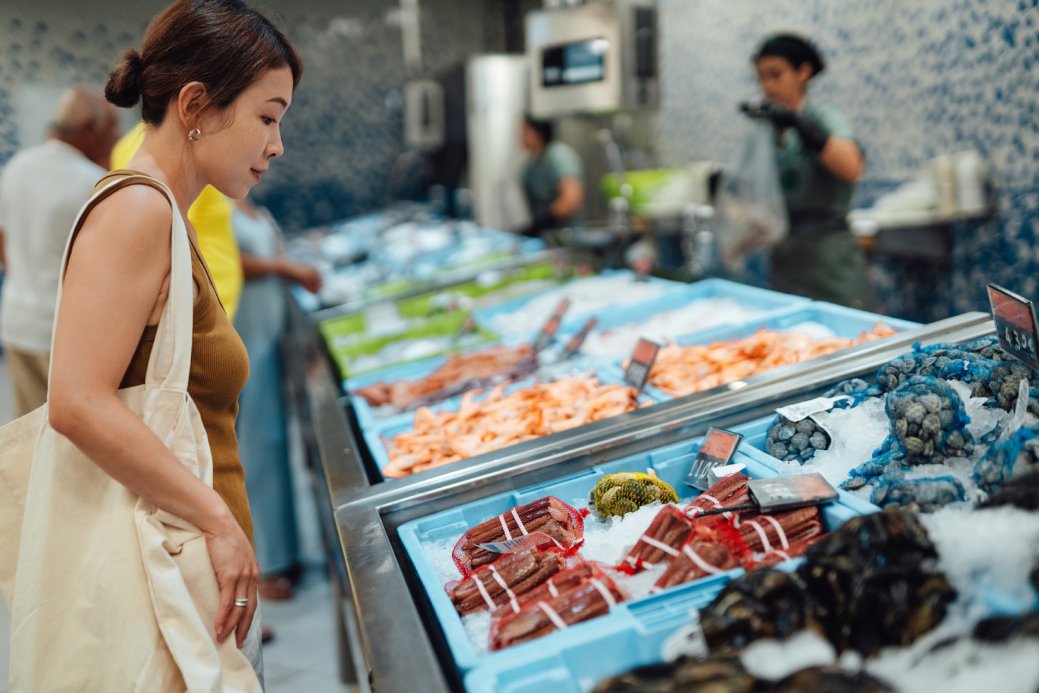 A young Asian woman is choosing fresh seafood at supermarket.