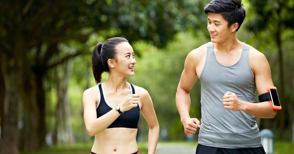 Hai người đang chạy bộ ngoài trời, trò chuyện vui vẻ trong công viên xanh mát.