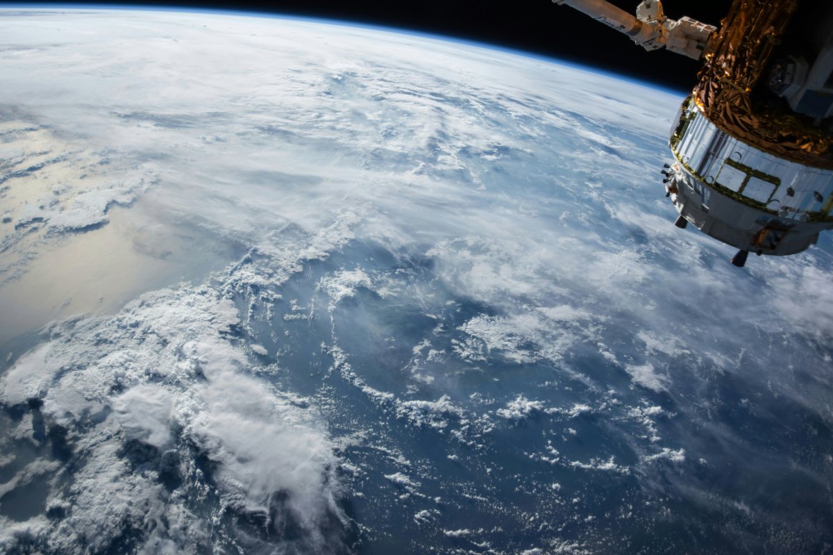 A view of Earth from space, showcasing the planet's curvature with a space station visible in the background.