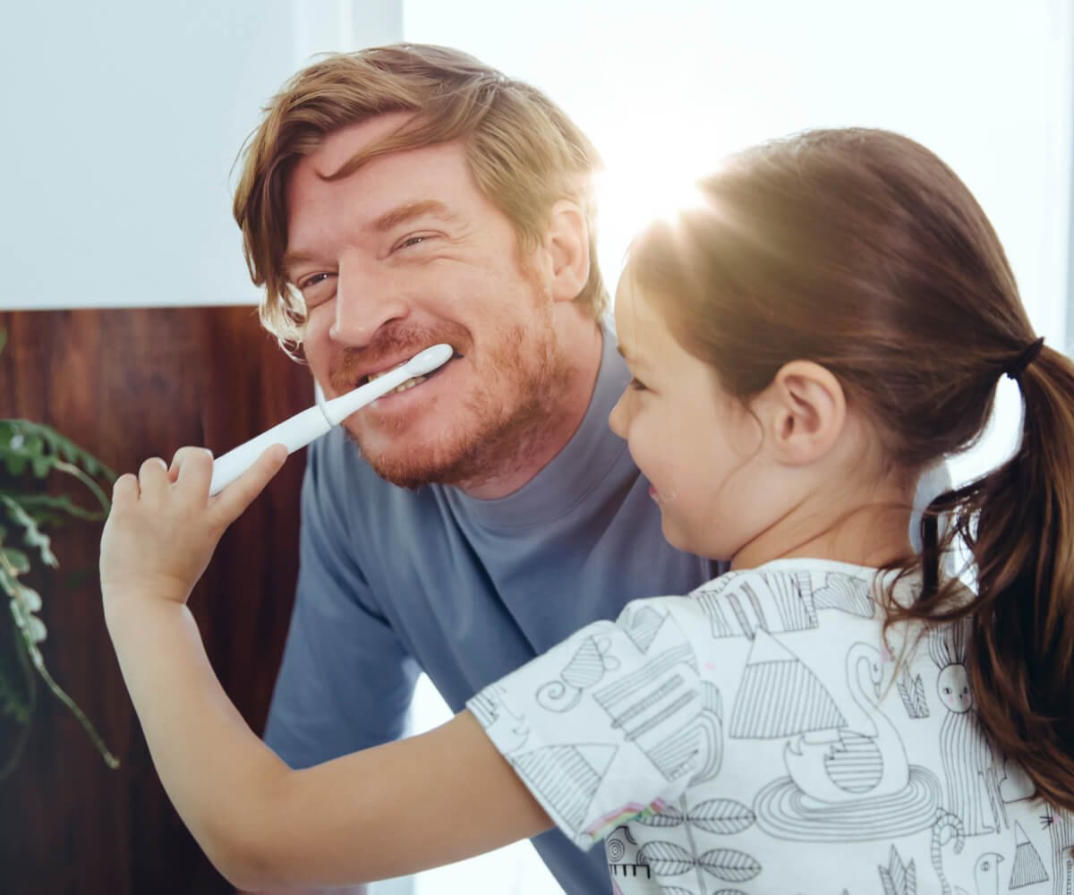 A man and a young girl are brushing their teeth together