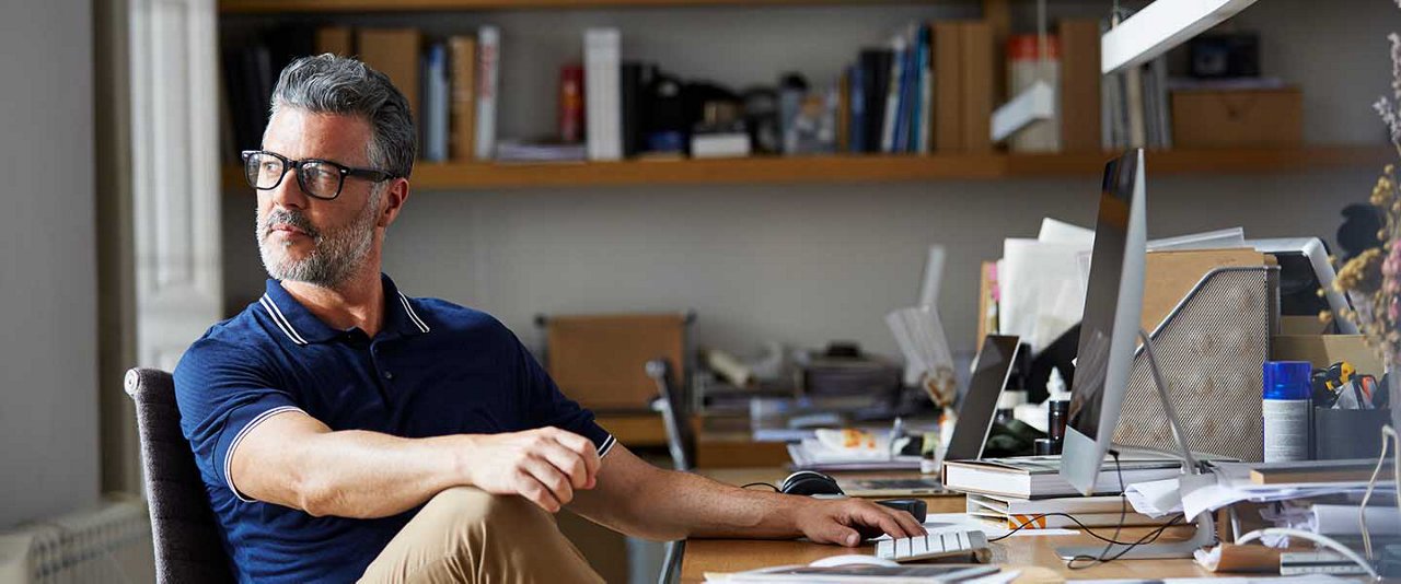 Man sitting at work desk looking out while thinking