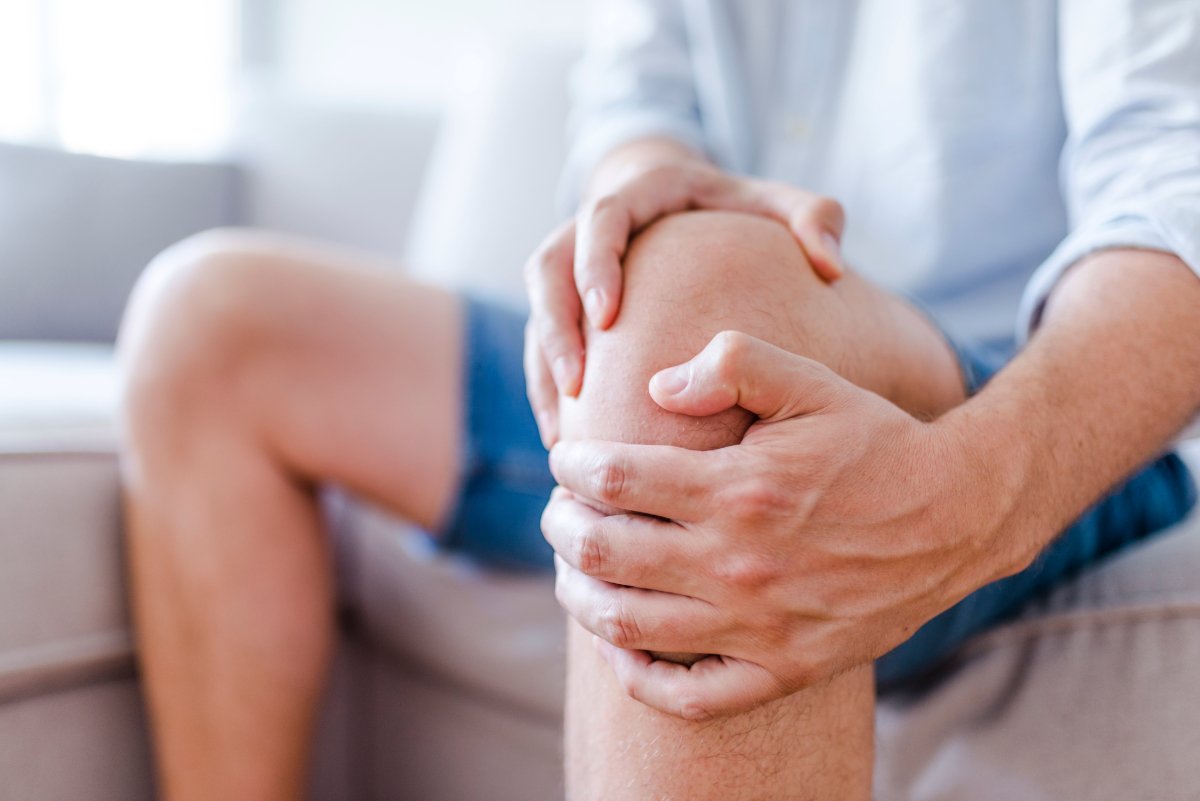 A man experiencing knee pain sits on a couch