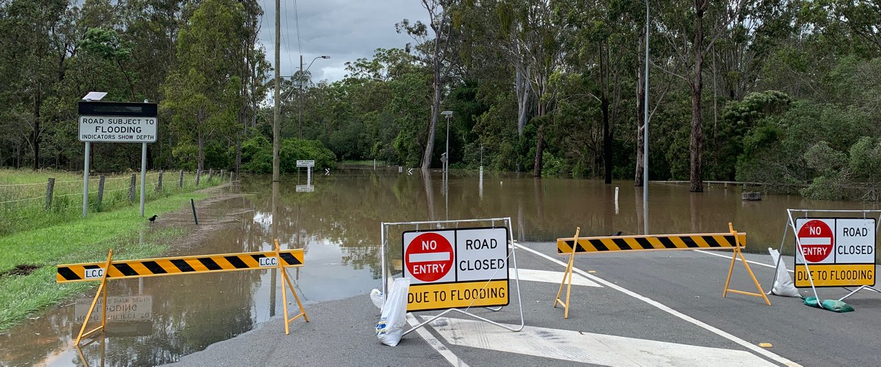 A flooded road with warning signs and barricades indicating unsafe conditions for vehicles and pedestrians.