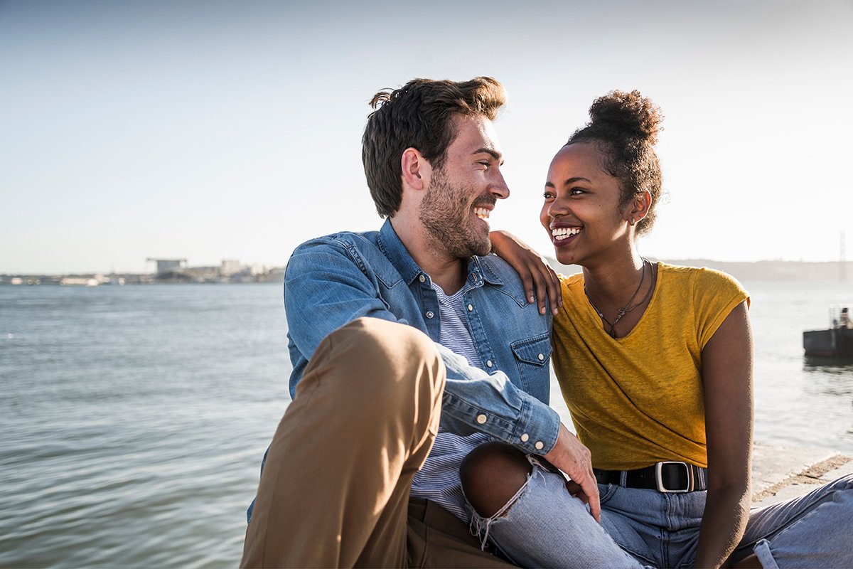 A young couple enjoys a serene moment together, sitting on a dock by the calm water, surrounded by nature's beauty.