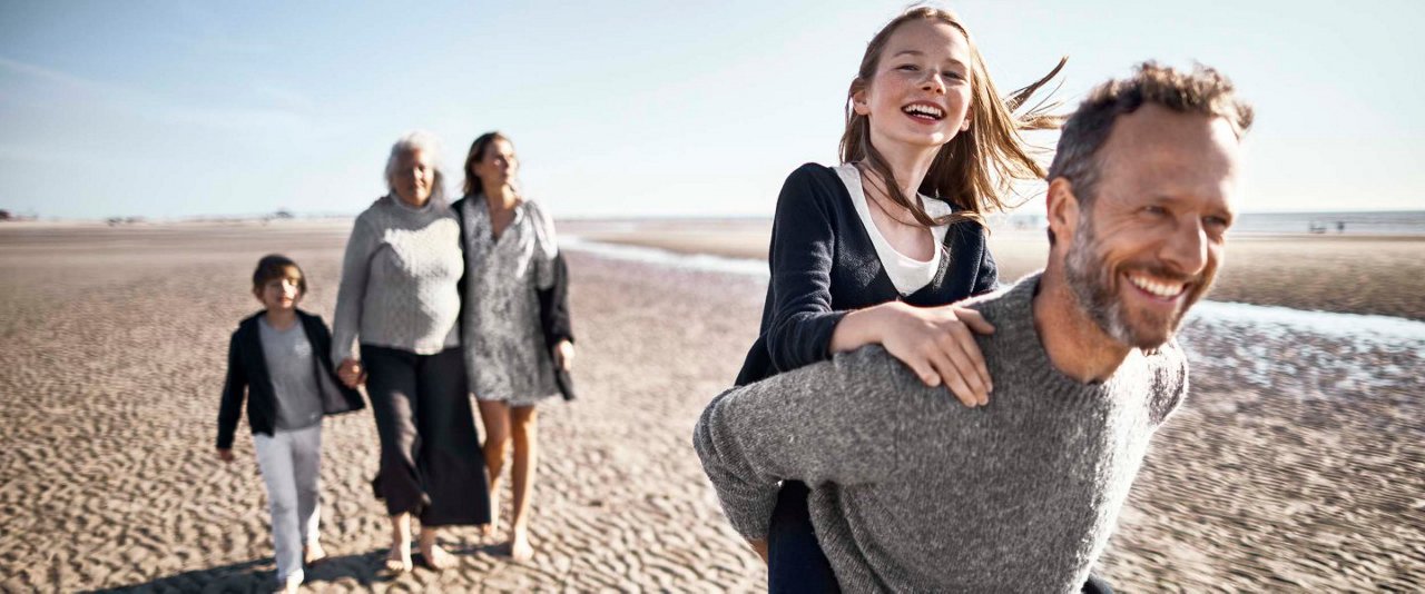 Family on beach with dad giving piggyback