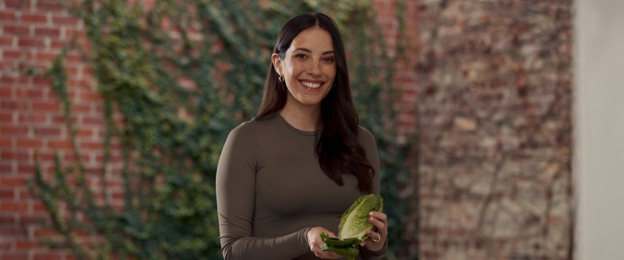 A woman holding a green vegetable, with a focused expression on her face.