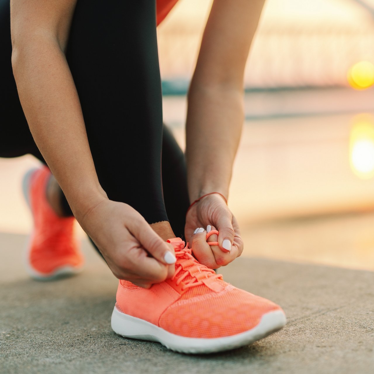 Close up of sporty woman tying shoelace while kneeling outdoor, In background bridge. Fitness outdoors concept.