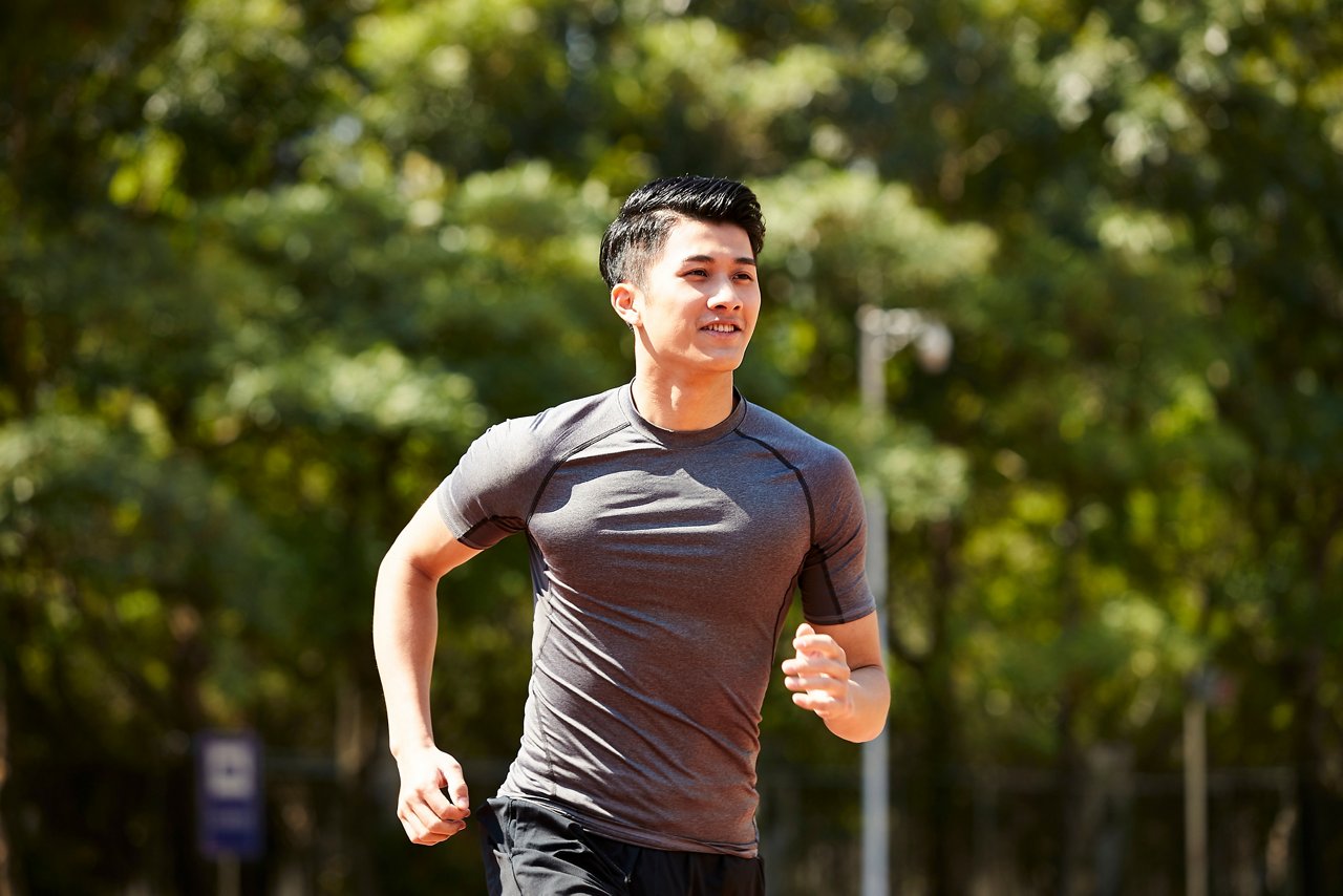 Young Asian man smiles as he runs outdoor