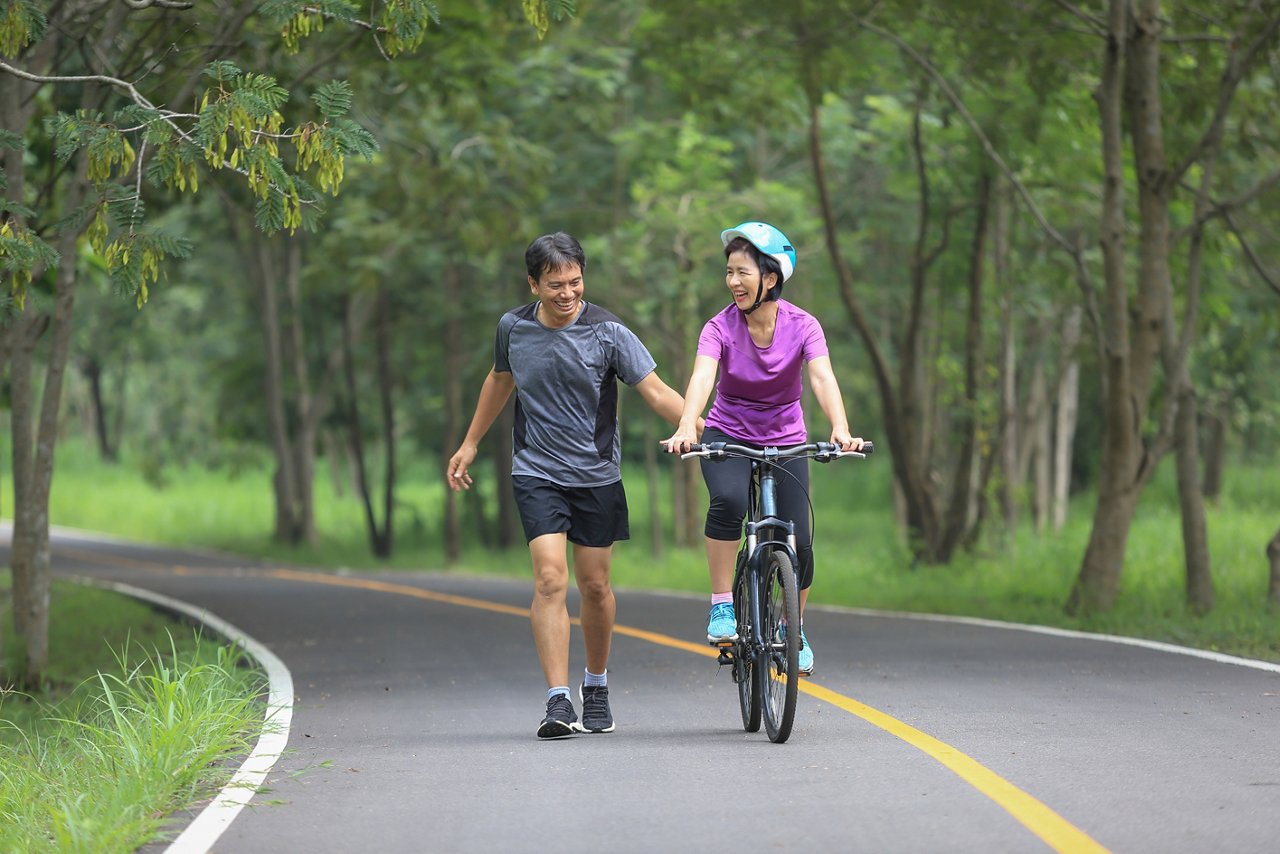 A woman rides a bicycle while a man jogs beside her.